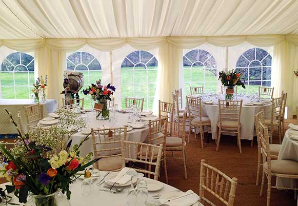 Corner of a traiditionally styled flowery wedding marquee with coconut matting on the floor and Georgian windows.